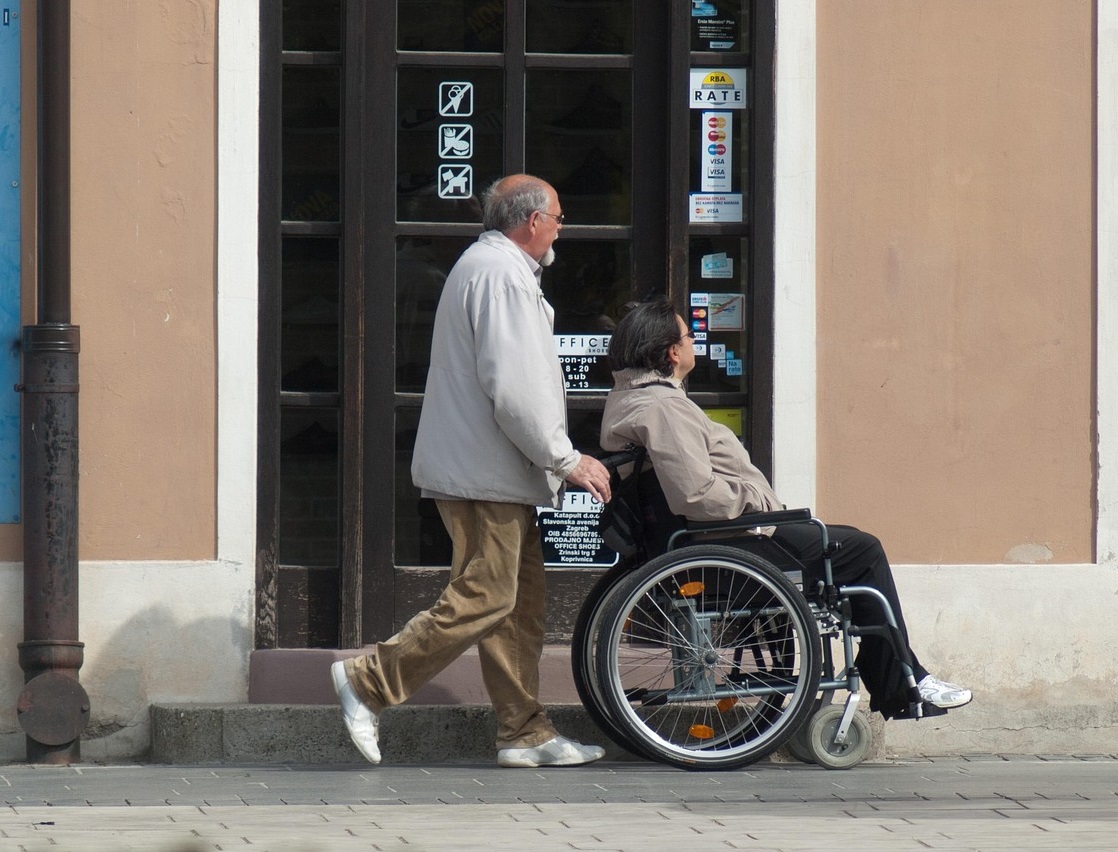 mężczyzna pcha wózek z niepełnosprawną kobietą